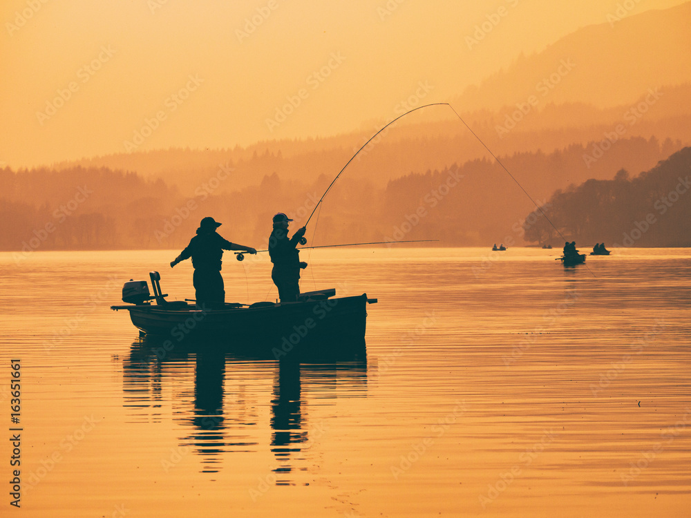 Silhouette of man fishing on lake from boat at sunset. Lake of Menteith, Stirlingshire, Scotland, UK
