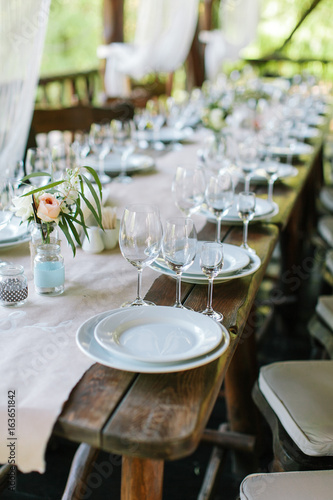 Glasses and plates on the festive wooden table. Wedding table decor concept. Table setting in classic style, setout. fine art.