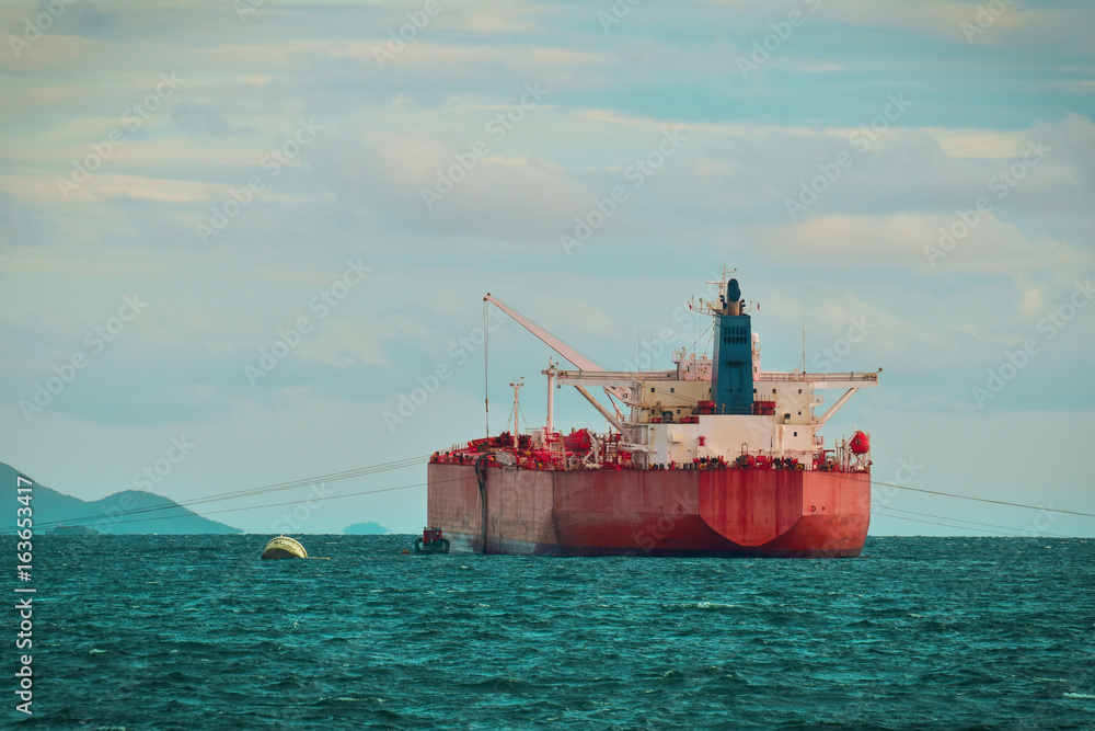 Large cargo vessel anchoring in open sea with island background. Cargo shipping and logistics. Large cargo vessel anchoring in open sea with island background. Cargo shipping and logistics.