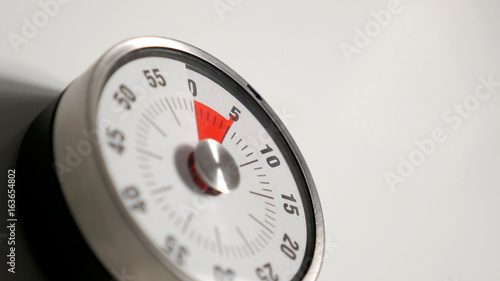 Classical vintage kitchen countdown timer close up shot with analog clock face and red remaining time display, 5 minutes left, low depth-of-field with blur