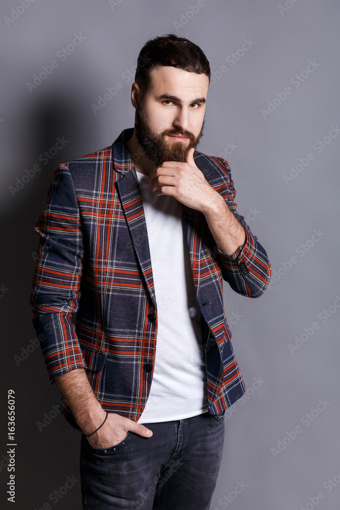 Puzzled young man stroking beard looking at camera Puzzled young man stroking beard looking at camera