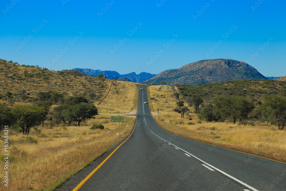 Namibian road through the savannas and deserts with markings and traffic signs. Namibian road through the savannas and deserts with markings and traffic signs.