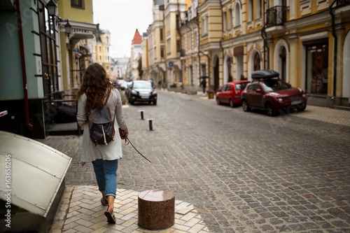 View on a city street with woman walking on a sidewalk. Travelgirl taking a walk in european city.