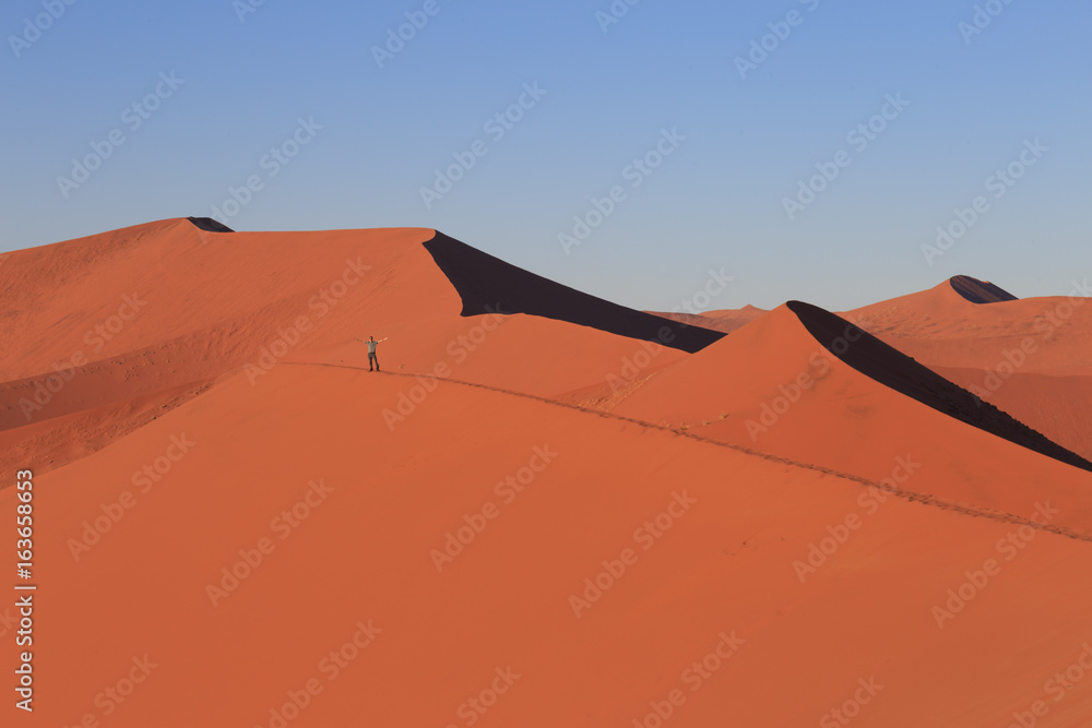Man  on sand dune in desert during sunrise.  Sossusvlei, Namib Naukluft National Park, Namibia