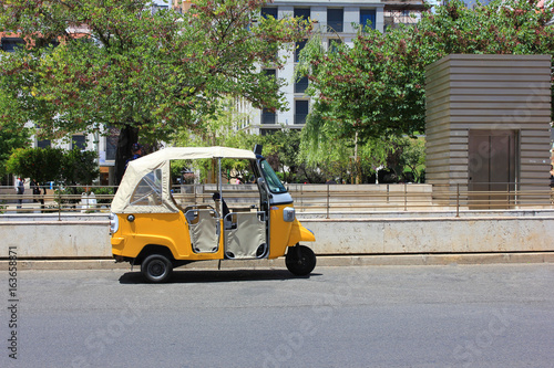 Tuk tuk small passenger three weel mini car isolated on summer empty street road background. Bright yellow rickshaw driven by locals helps tourists to travel around the city fast and cheaper than taxi photo