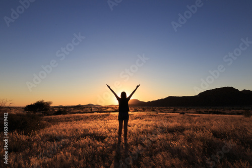 Silhouette of woman open arms under the sunset at african savanna landscape.