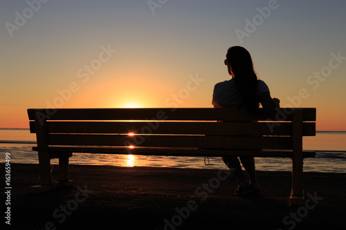 The silhouette of a lonely girl sitting on a bench watching the sunset