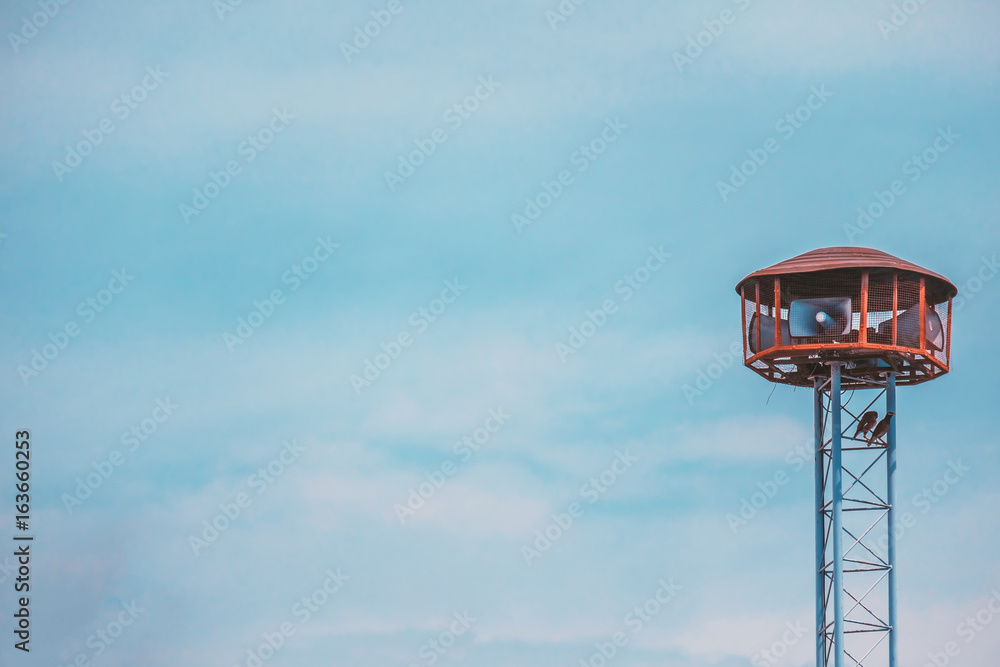 Public speaker tower with two birds perching  on against blue sky background and added retro color filter