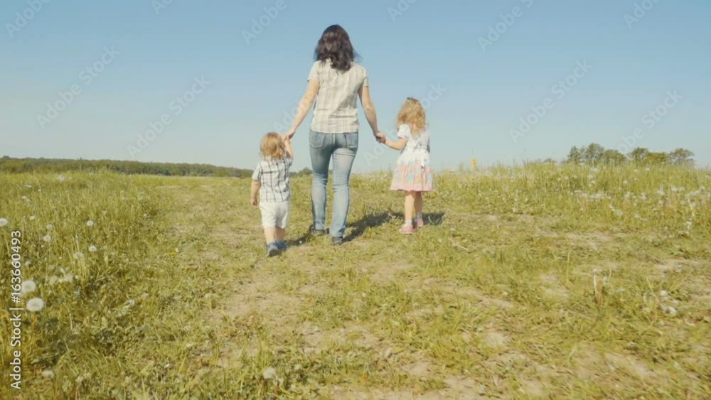 Family mother with her son and daughter are walking around the field. Walk in the fresh air. Summer sunny day. Slow Motion. Family mother with her son and daughter are walking around the field. Walk in the fresh air. Summer sunny day. Slow Motion.