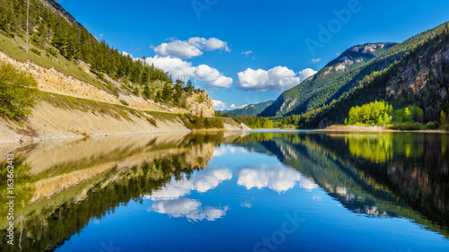 Reflections of blue sky, trees and mountains in the smooth surface on the crystal clear water of Crown Lake, along Highway 99 in Marble Canyon Provincial Park in British Columbia, Canada