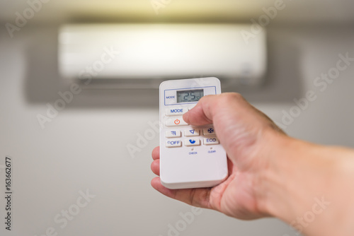 Open room air conditioner with remote control. Hand holding remote control of room air conditioner.