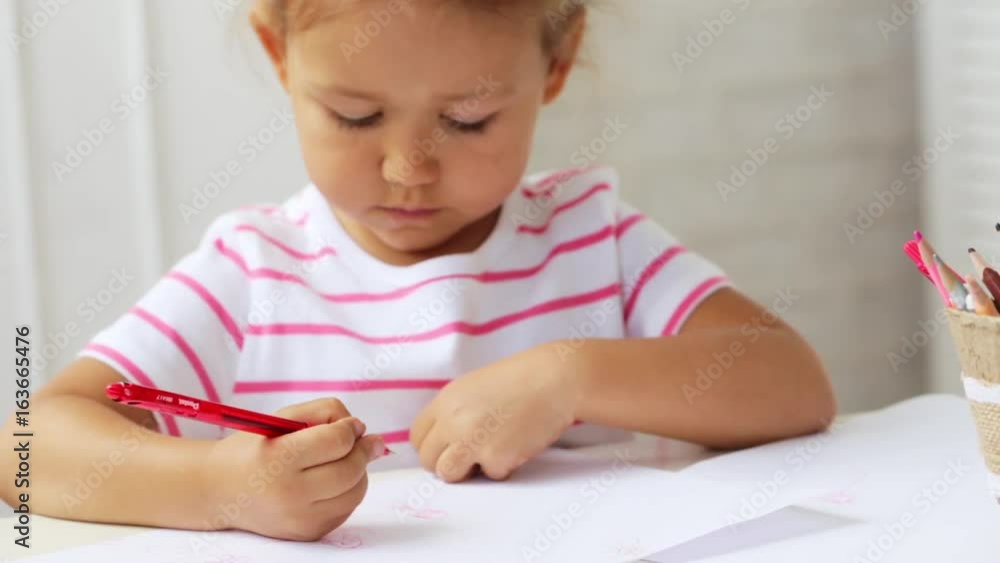 Cute preschool girl sitting by the white table focused on drawing something. Cute preschool girl sitting by the white table focused on drawing something.