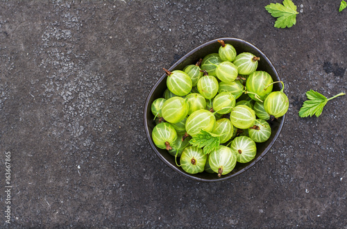 Fresh green gooseberries in a ceramic bowl on a dark background. Top view photo
