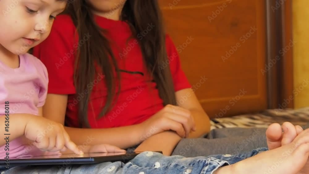 Children with a tablet. Two sisters play with the tablet. Children with a tablet. Two sisters play with the tablet.