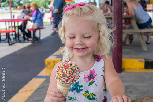 Smiling blond girl eating ice cream cone with sprinkles on top