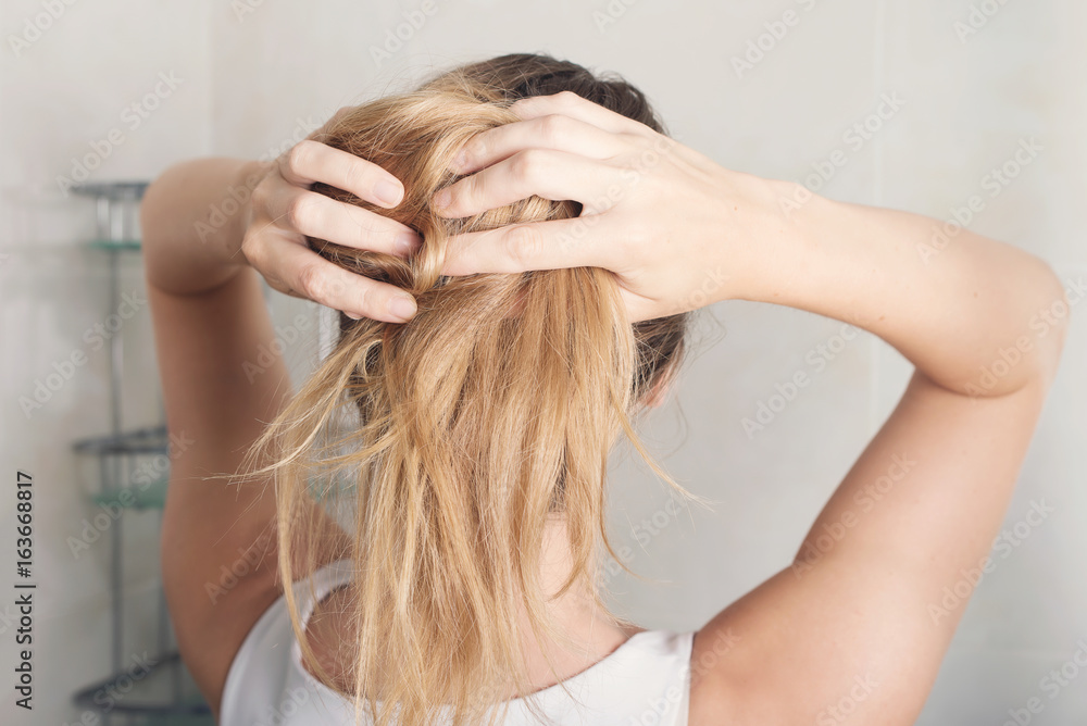 Beautiful young woman is styling hair in bathroom at home Beautiful young woman is styling hair in bathroom at home