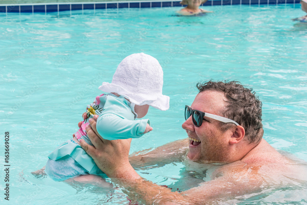 Young smiling man holding baby girl in the swimming pool