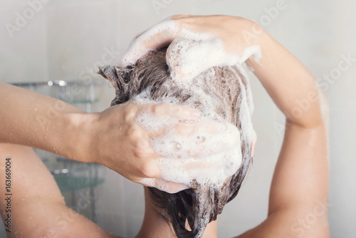 Beautiful young woman is washing hair in bathroom at home