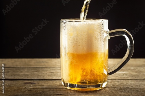 Pouring beer into a glass on a wooden table. Alcoholic beverages. Alcohol-free beer. Sale of beer to the bar.