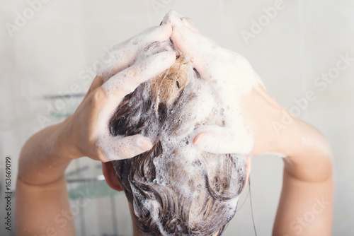 Beautiful young woman is washing hair in bathroom at home