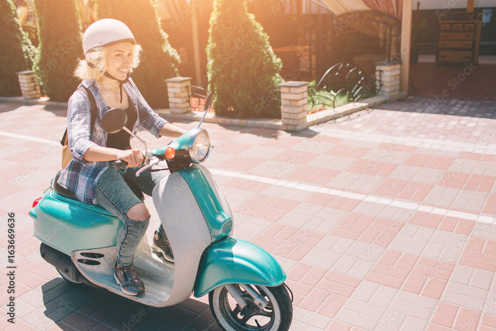 Obraz premium Młoda wesoła dziewczyna jazdy skuterem w mieście. Portret młodej i stylowej kobiety z motoroweru.