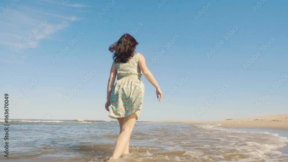 Attractive young woman in a dress strolls along the seacoast barefoot and enjoys herself. Beach with white sand. Outgoing coastal line. Slow Motion. Attractive young woman in a dress strolls along the seacoast barefoot and enjoys herself. Beach with white sand. Outgoing coastal line. Slow Motion.