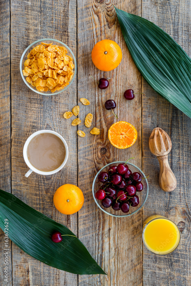 Light tasty breakfast. Muesli, oranges, cherry, french croissant and milky coffee on wooden table background top view