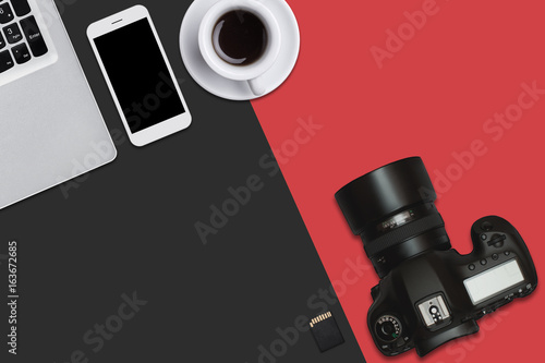 Top view of laptop, smart phone, flash card, camera and cup of coffee lying on red and black surface. Workplace of talented photographer with modern supplies and modern equipment for his work