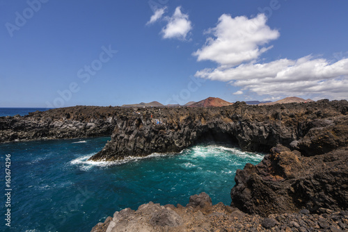 Los Hervideros lava cave in the turquoise sea with volcano in the background - the unique volcanic landscape of Lanzarote and popular touristic attraction, Canary islands, Spain