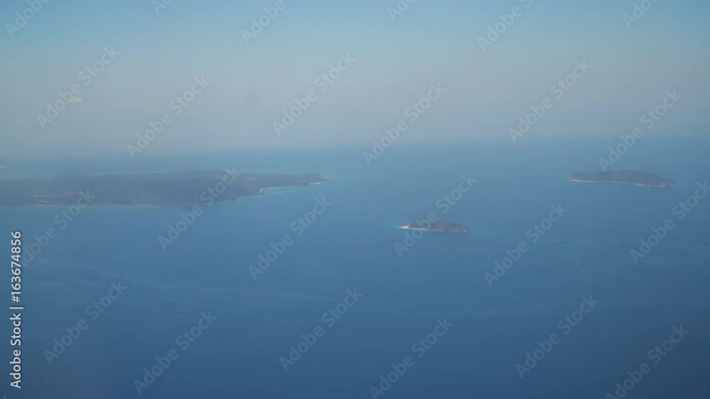 View through an airplane window on the tropical island, ocean, sky and clouds. Aerial view sea, clouds and sky as seen through window of an aircraft. 4K video. Aerial footage. Travel concept.