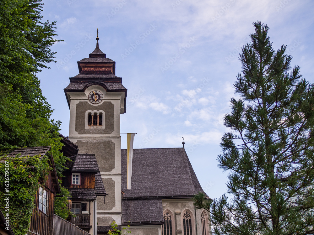 Catholic Parish Church in Hallstatt Austria with Trees Wooden Buildings and Blue Sky