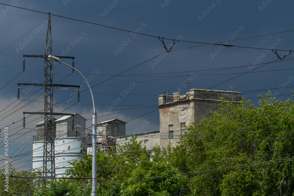 Thunderclouds over the buildings of an industrial factory. Old walls and wires of a high-voltage line
