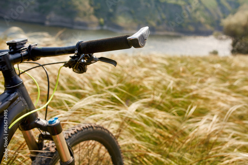 Close-up of the handlaber of mountain bicycle against beautiful landscape in summer season.