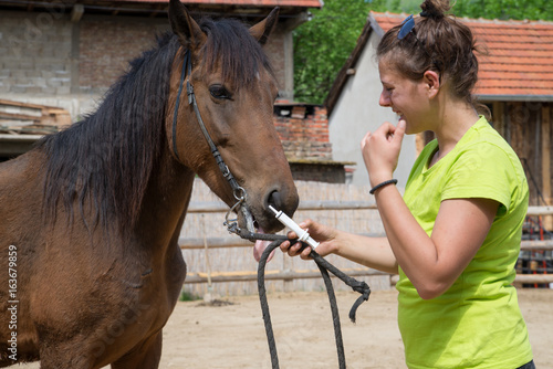 Young veterinarian girl on a farm giving a medicine to a horse