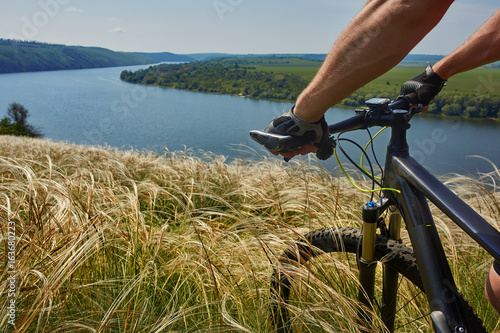 Close-up of the cyclist holding bicycle on the meadow in the countryside against beautiful landscape. photo