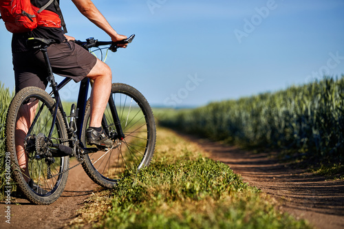 Fototapeta Naklejka Na Ścianę i Meble -  Close-up of cyclist man legs with mountain bike on the path of the green field in the countryside.