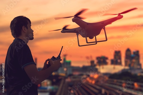 Silhouette of man controlling a drone at sunset. City in background.