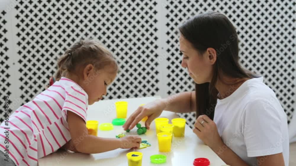 Young attractive mother with little cute daughter play with modeling clay Young attractive mother with little cute daughter play with modeling clay