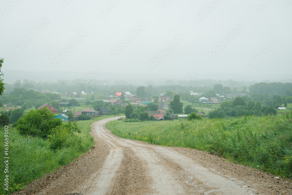 Fototapeta premium gravel road to a small village in the fog