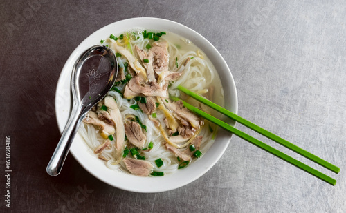 pho ga, vietnamese chicken rice noodle soup with chicken, herbs.on a table from scratched aluminum