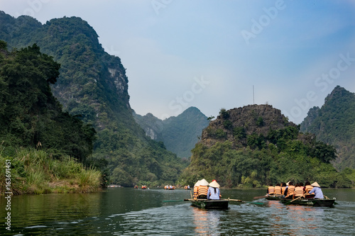 Tourists traveling in small boat along the River at the Trang An portion, Ninh Binh Province, Vietnam. Landscape formed by karst towers and plants along the river. Reed.