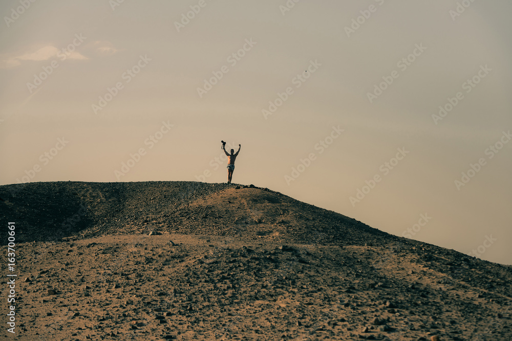 Man with camera and winner gesture on desert hill top
