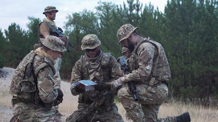 Two soldiers sitting in nature and using map and gps tracker for navigation.