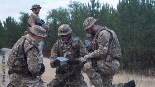 Foto Two soldiers sitting in nature and using map and gps tracker for navigation