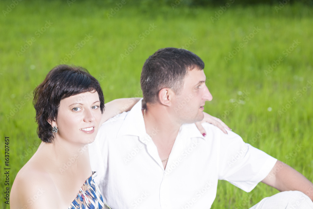 Family Relationships Concepts. Portrait of Caucasian Couple Relaxing Together Outdoors on Grass in Park. Sitting Embraced Family Relationships Concepts. Portrait of Caucasian Couple Relaxing Together Outdoors on Grass in Park. Sitting Embraced