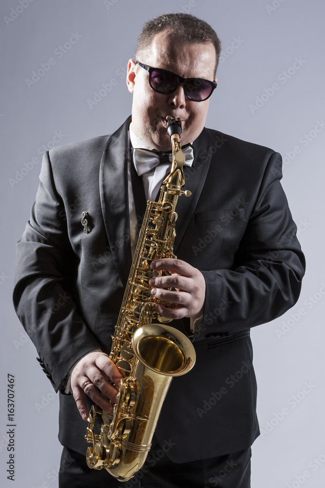 Naklejka premium Music Concepts. High Contrast Portrait of Caucasian Mature Expressive Saxophone Player Posing in Suit Against White Background.