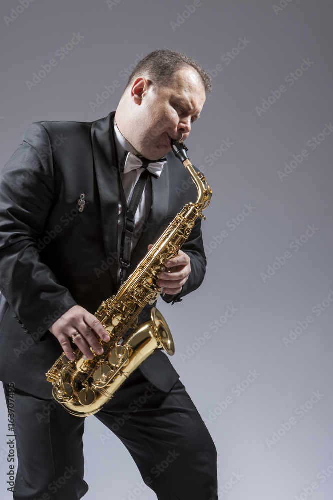 Naklejka premium Music and Musicians Ideas and Concepts. Portrait of Caucasian Mature Expressive Saxophone Player Playing the Instrument Against White Background.