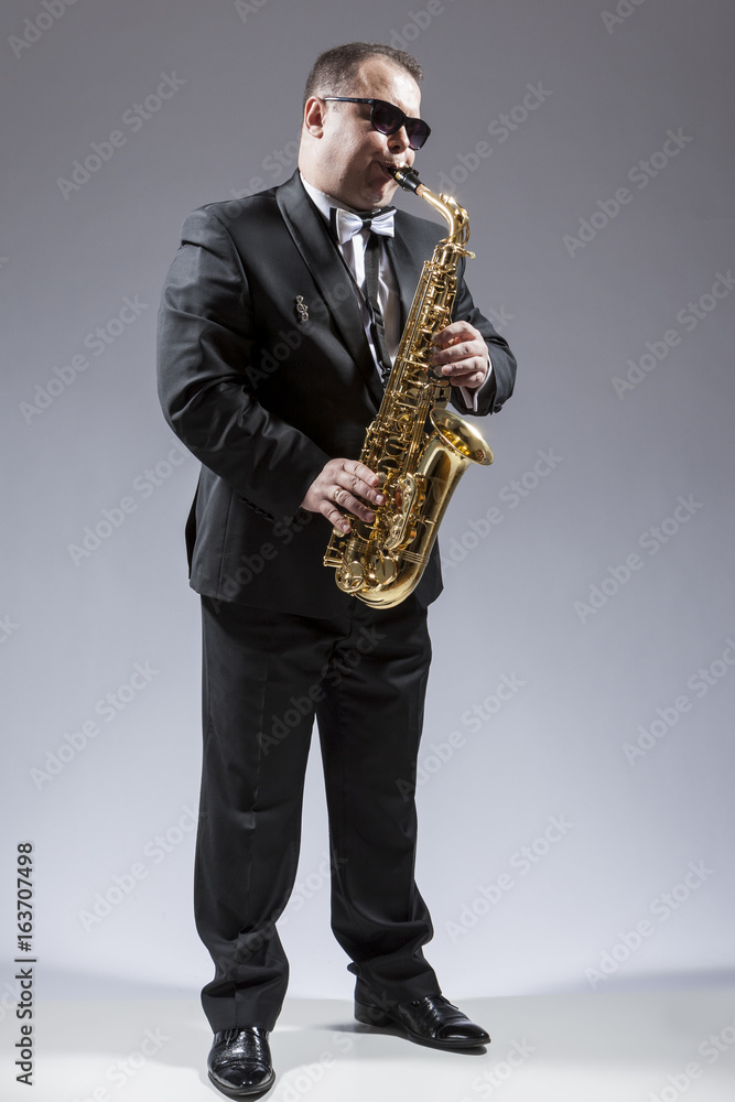 Fototapeta premium Music and Musicians Ideas and Concepts. Full Length Portrait of Caucasian Mature Saxophone Player in Sunglasses Playing the Instrument Against White.