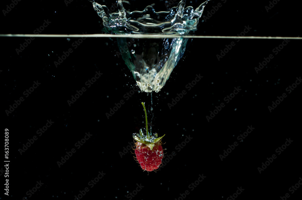 Raspberrie falling underwater with bubbles on black background