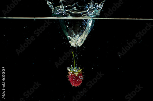 Raspberrie falling underwater with bubbles on black background